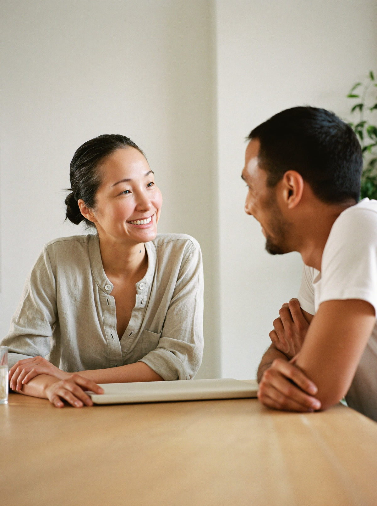 A nutrition coach and a client sit across a wooden table in a calm studio, both smiling mid-conversation.